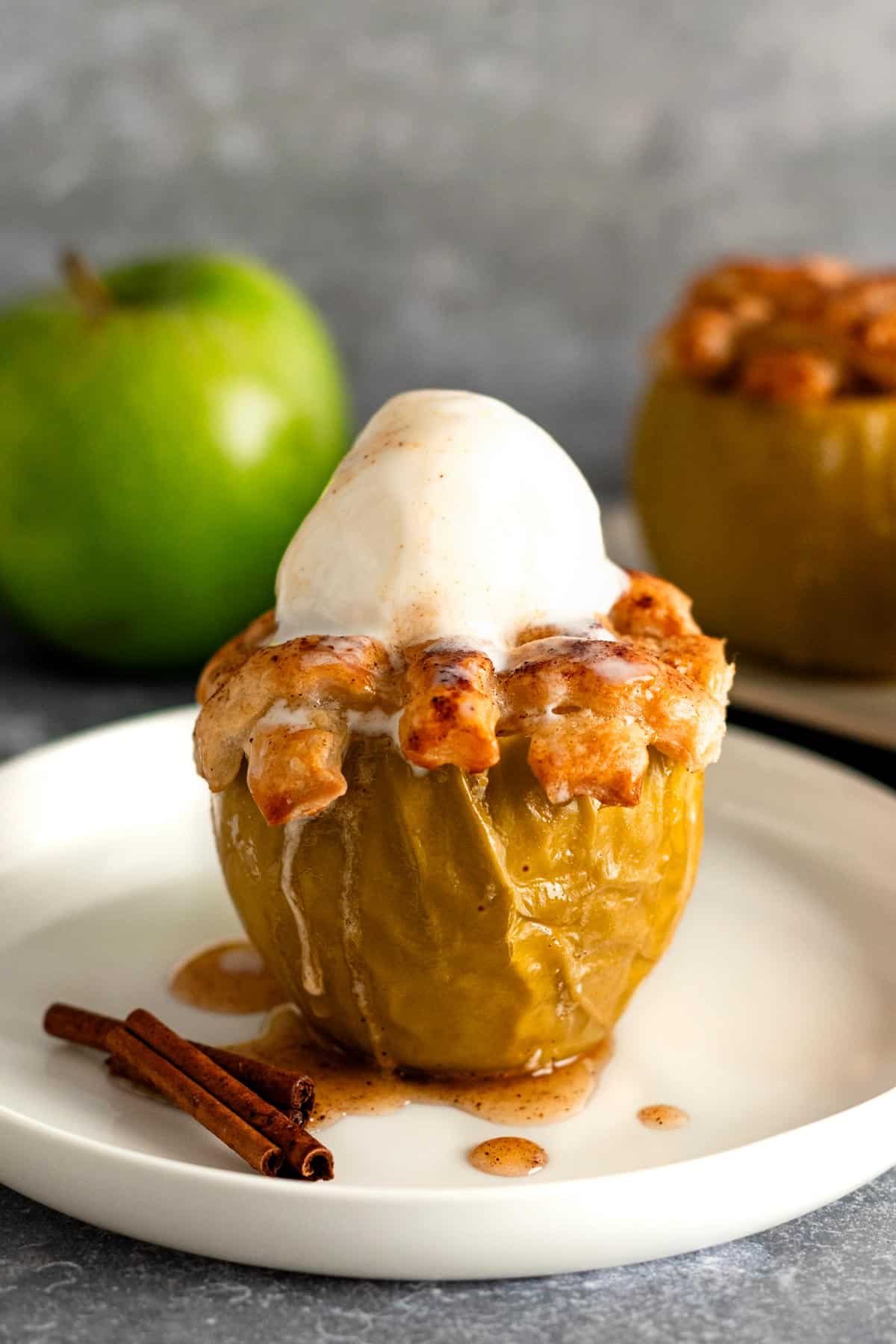 baked green apple on a plate with golden brown dough topping with vanilla ice cream.