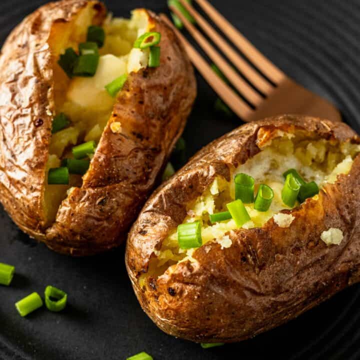 two air fryer baked potatoes cut in half topped with melting butter and chopped green onions.