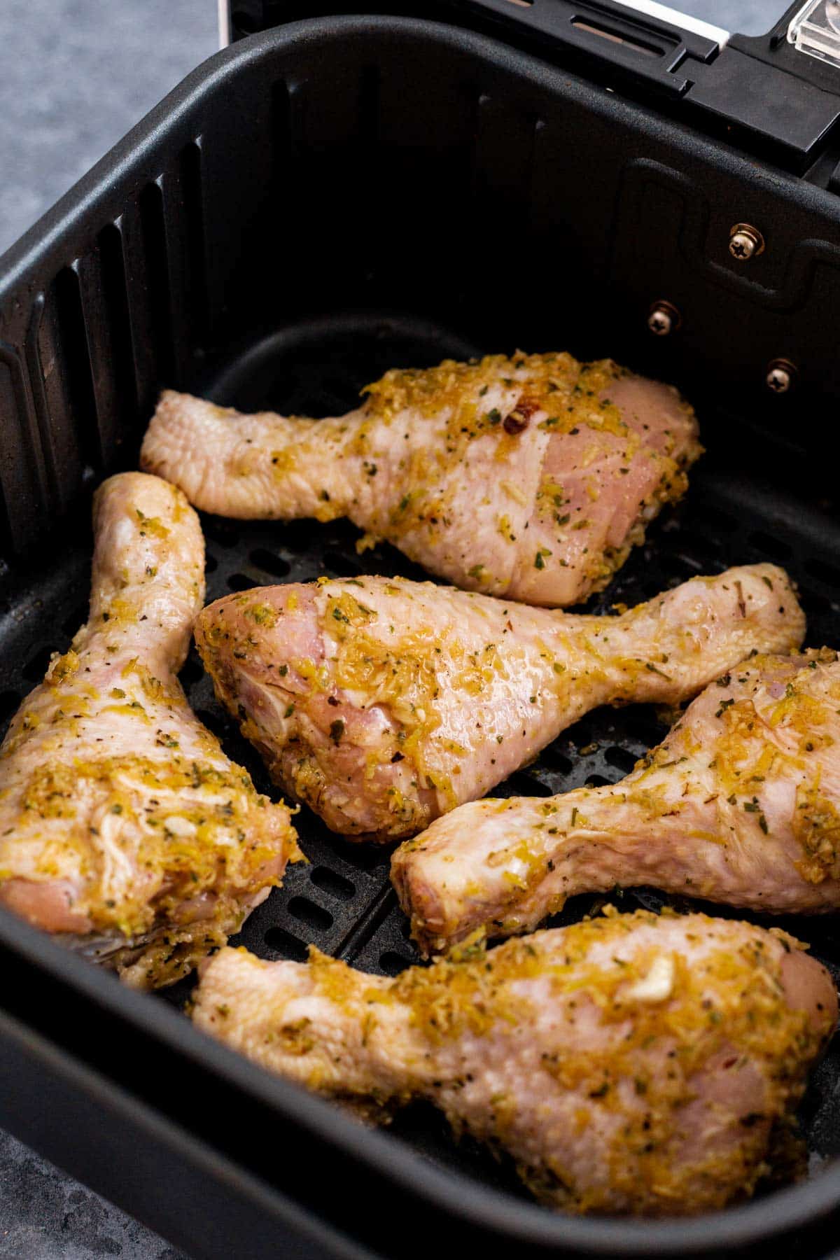 chicken legs in lemon garlic marinade in air fryer basket before cooking