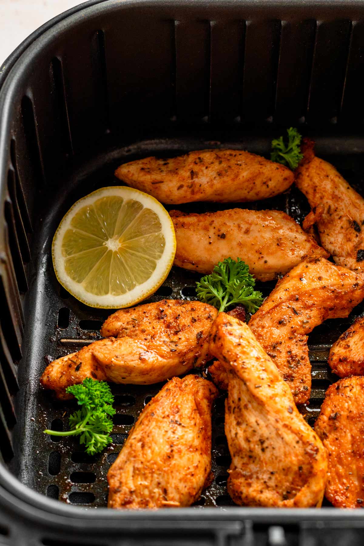 chicken tenders in air fryer with lemon slice.