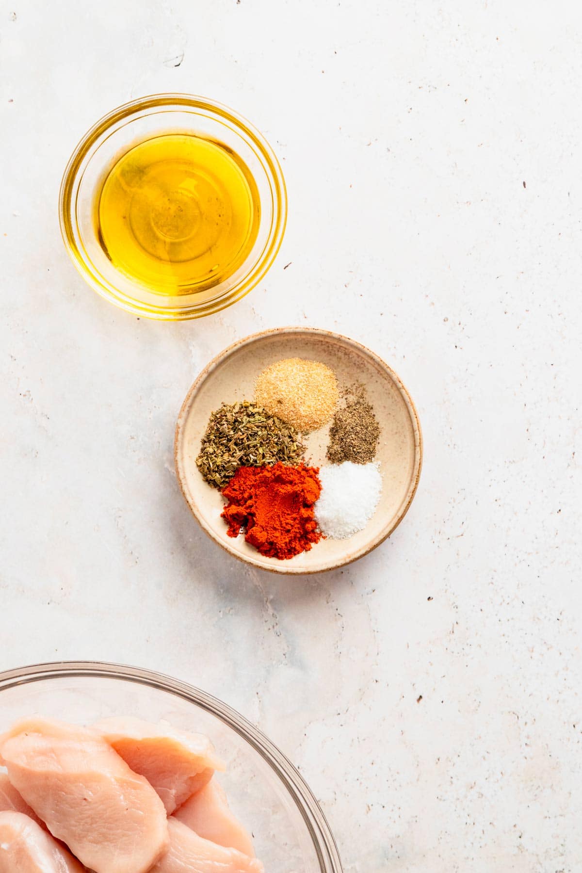 a bowl of seasonings, olive oil and chicken tenders.