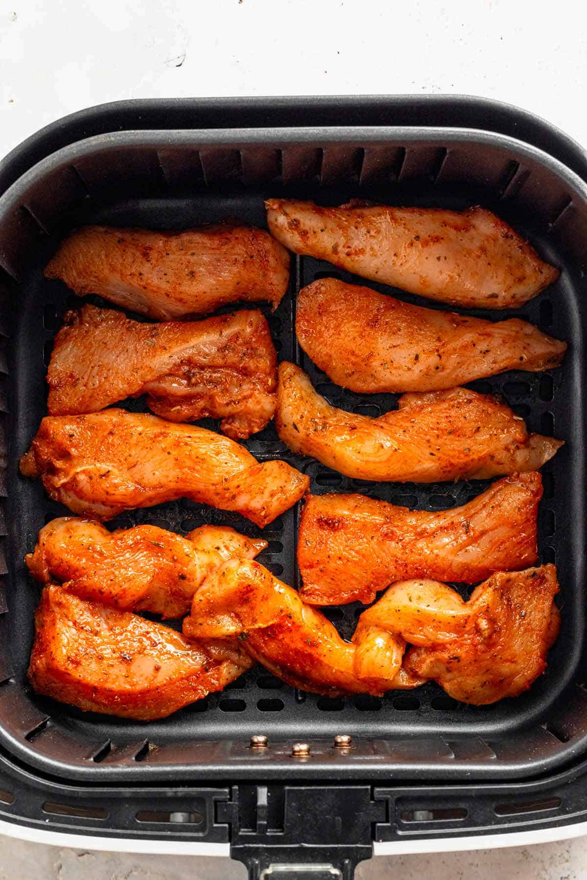 seasoned chicken tenders arranged in single layer in air fryer basket.