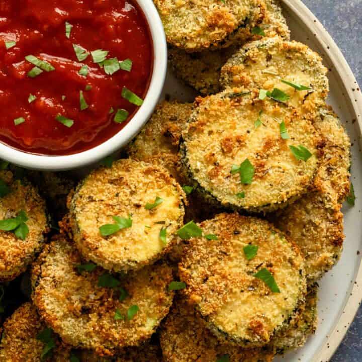 cooked air fryer zucchini slices on a bowl with red dipping sauce bowl.