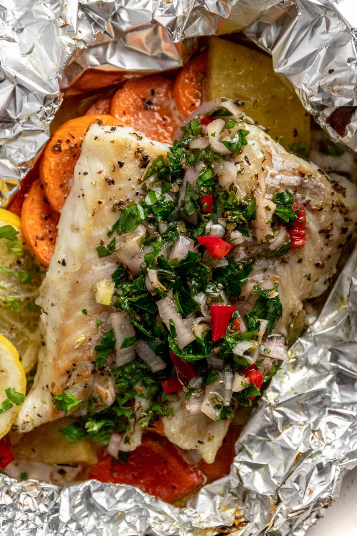 baked cod fillets in foil with chimichurri sauce, vegetables and lemon