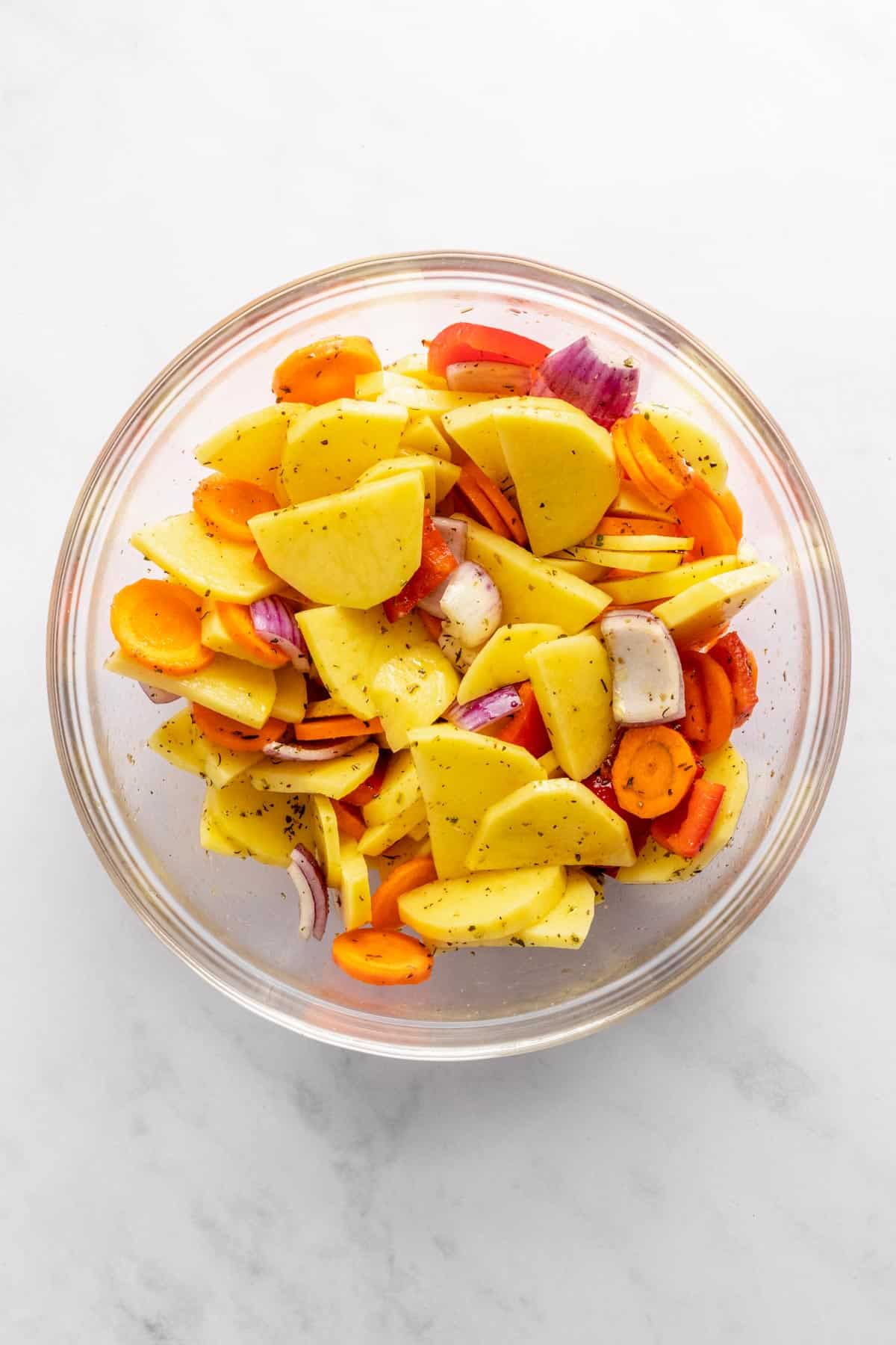 sliced vegetables mixed in a bowl with seasonings, herbs and olive oil