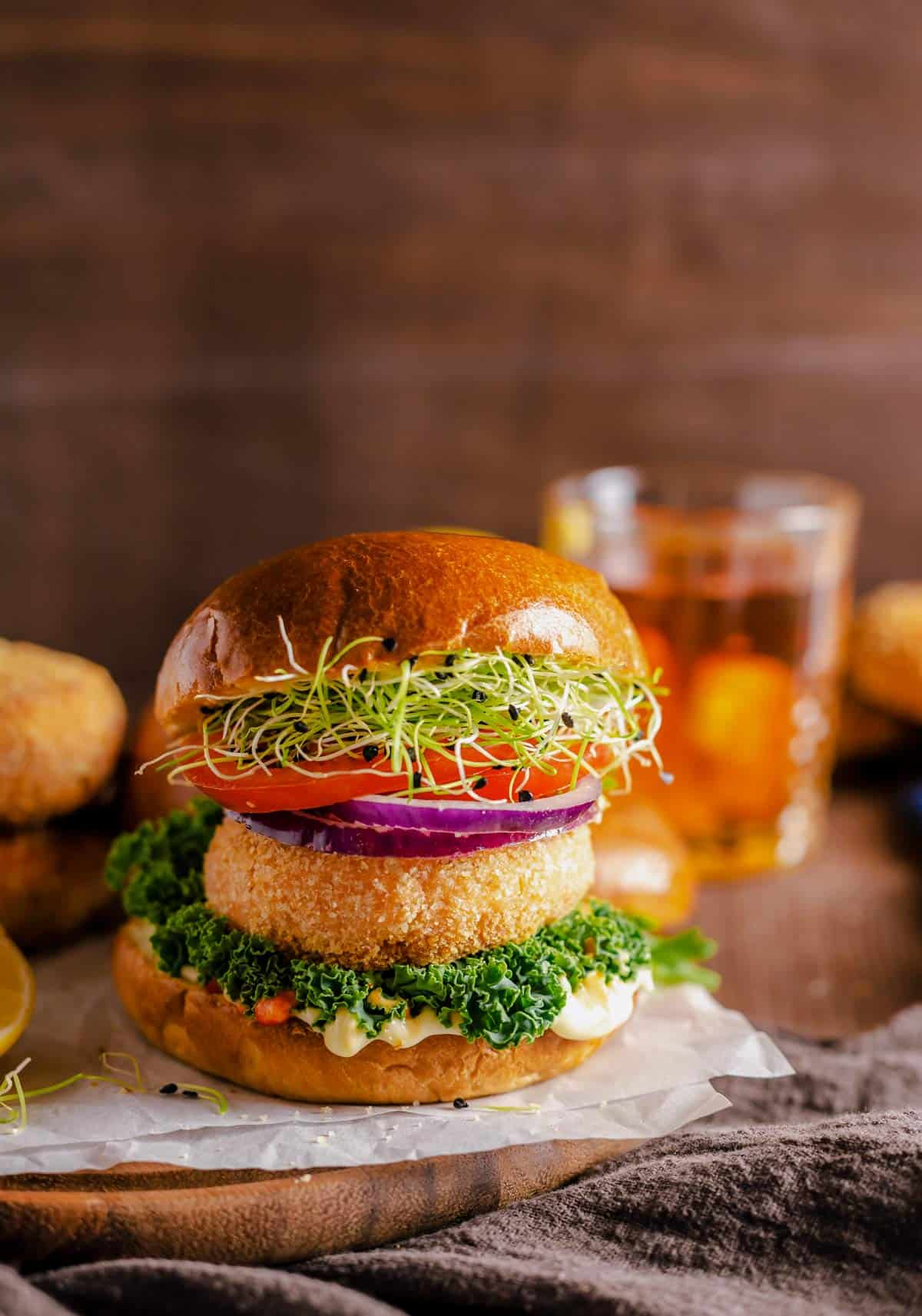 salmon patties served between burger buns, greens, tomato, red onion