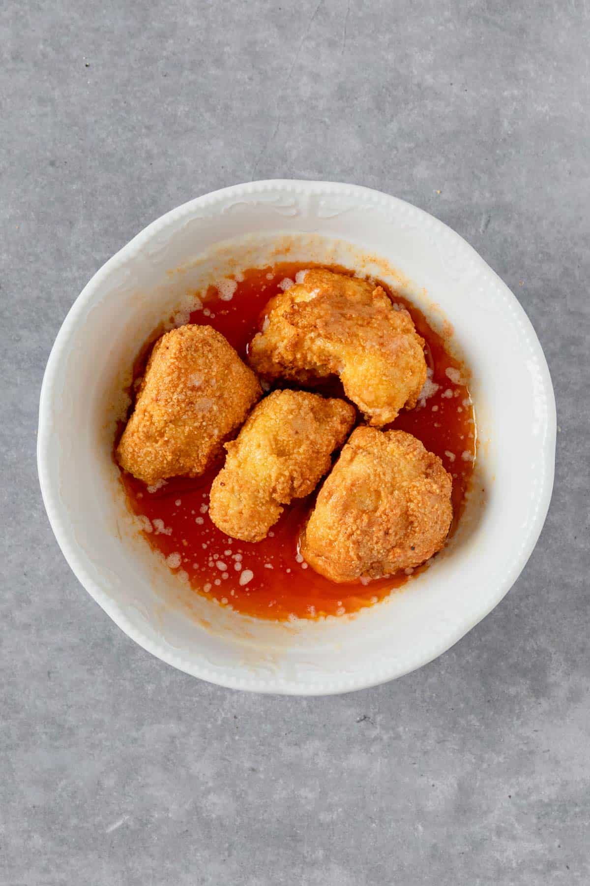 air fryer buffalo cauliflower dipped into hot sauce and butter bowl