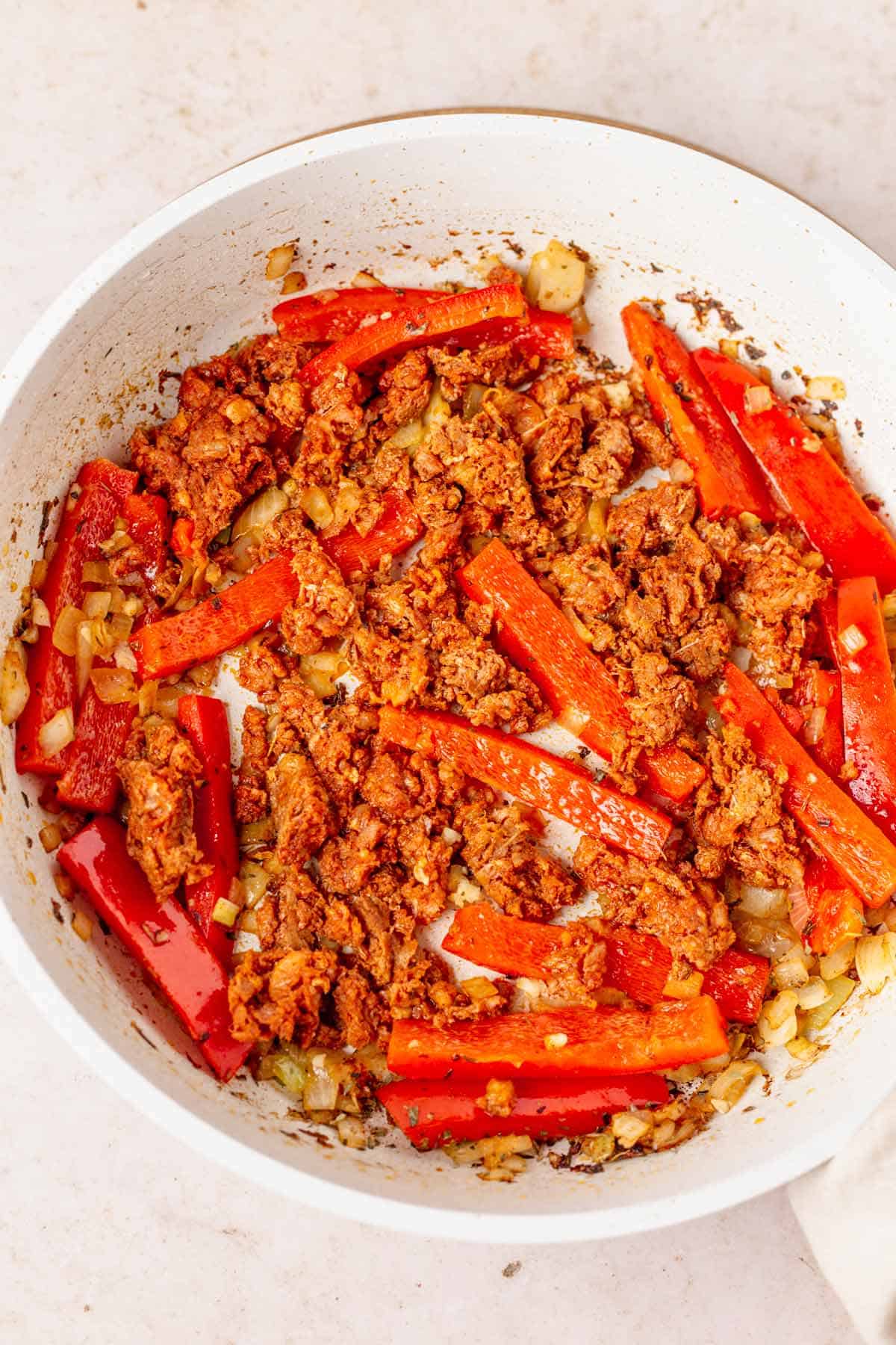 sausages frying with bell peppers in white skillet