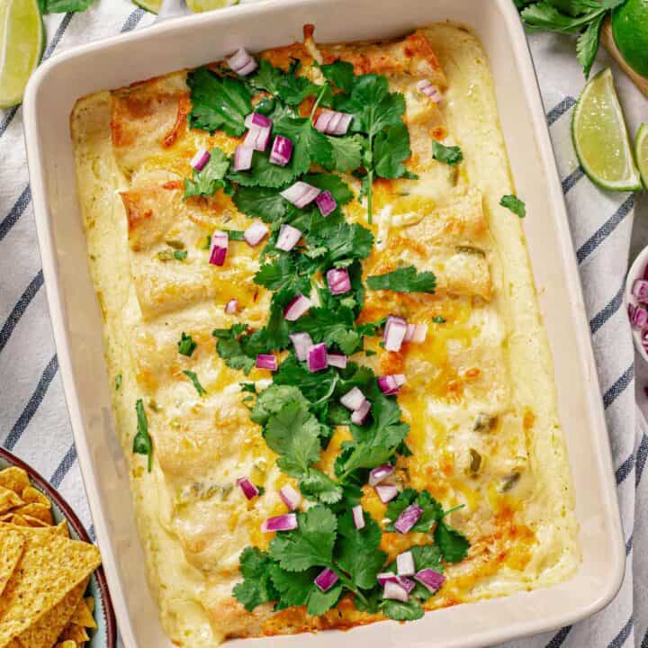 an over head shot of chicken enchilada in white sauce in a baking dish garnished with cilantro leaves and diced red onion in the middle