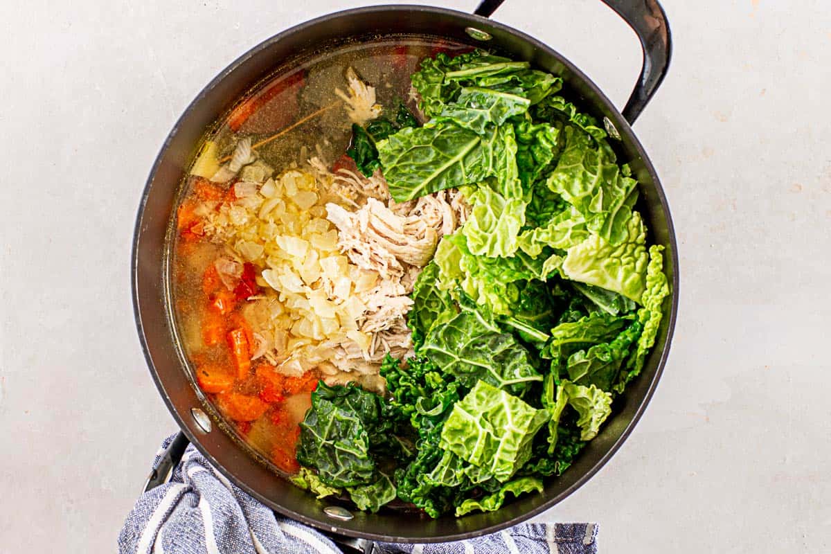 clear chicken soup with kale and vegetables in a black pot