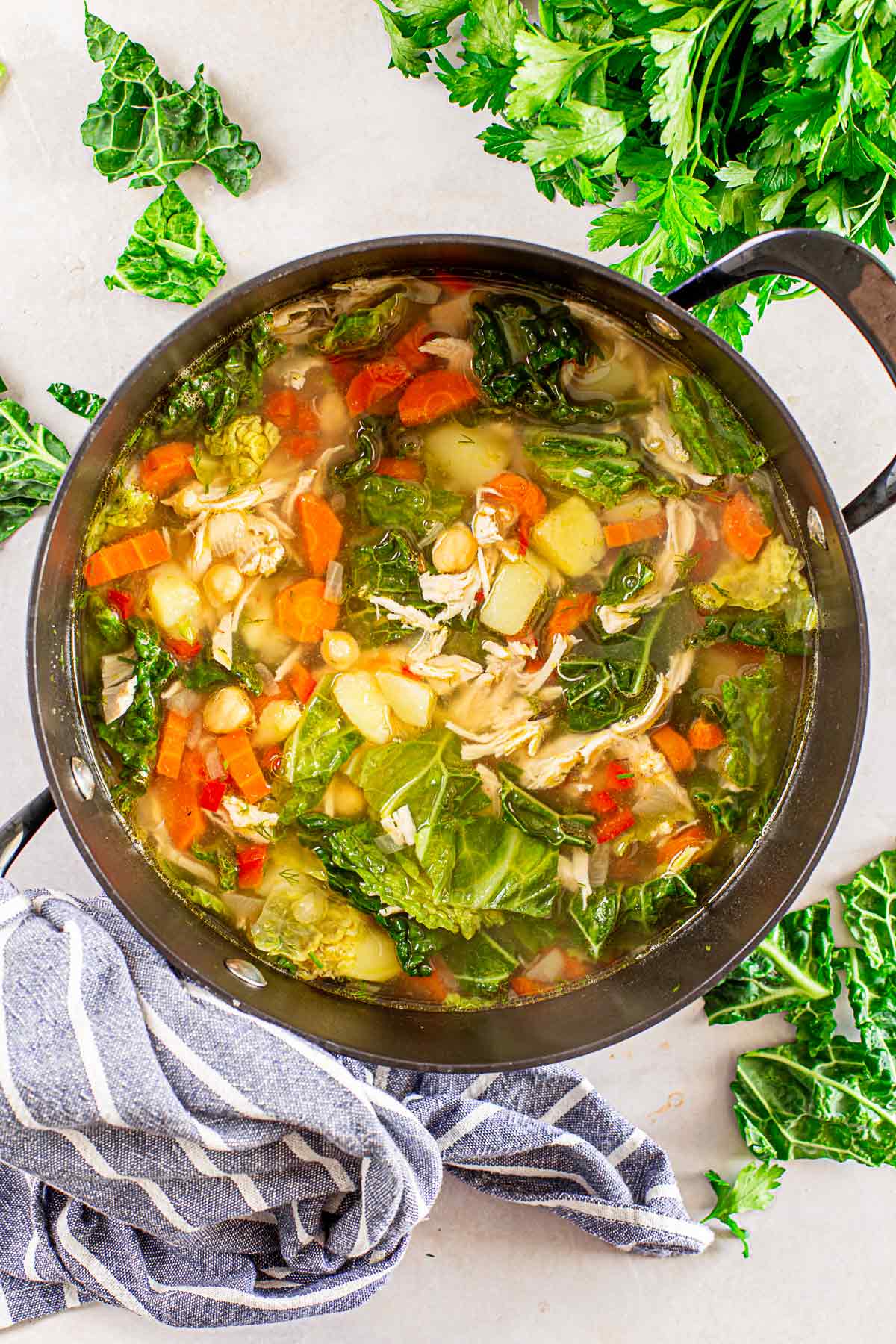 clear chicken soup with kale and vegetables in a black pot