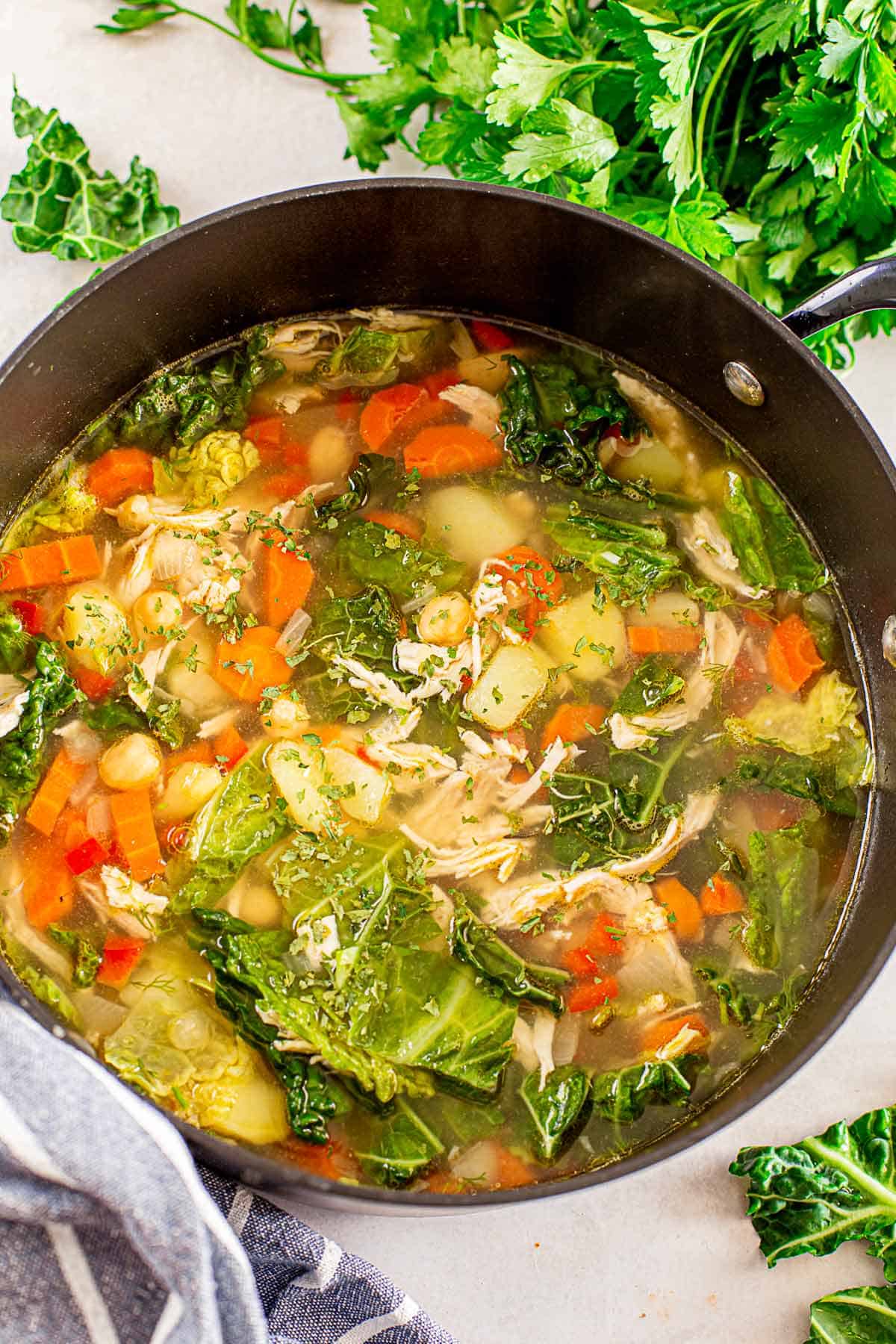 clear chicken soup with kale and vegetables in a black pot