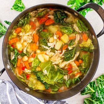 clear chicken soup with kale and vegetables in a black pot