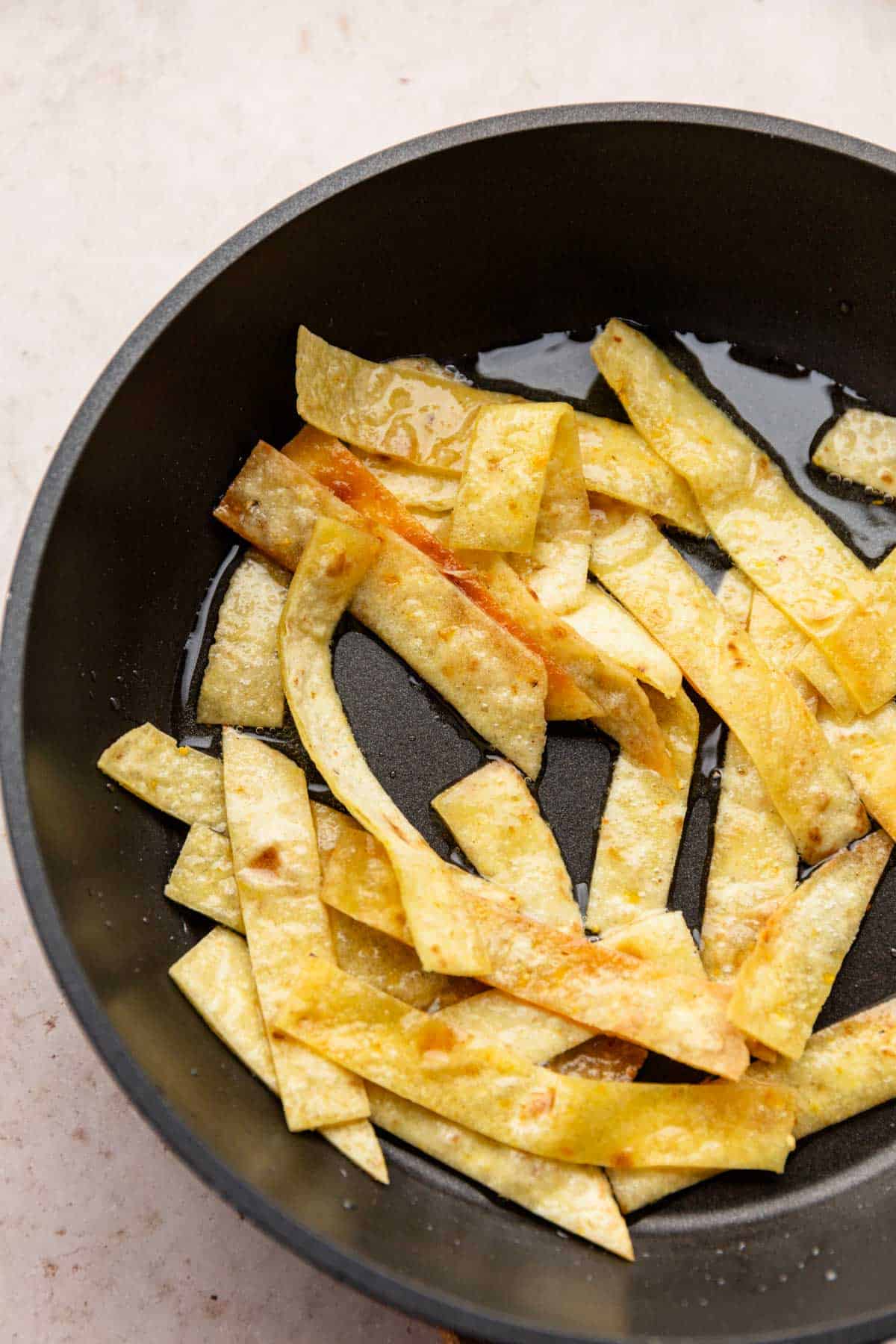 corn tortilla strips frying in skillet pan.