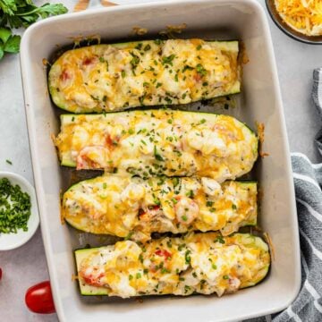 Stuffed zucchini boats filled with chicken parmesan and colby jack cheese in a white baking dish.