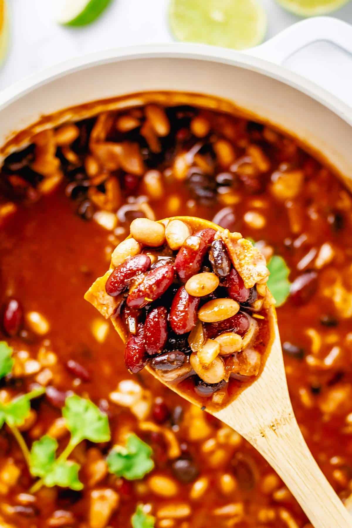 close up shot of cooked beans in tomato sauce on a wooden spoon