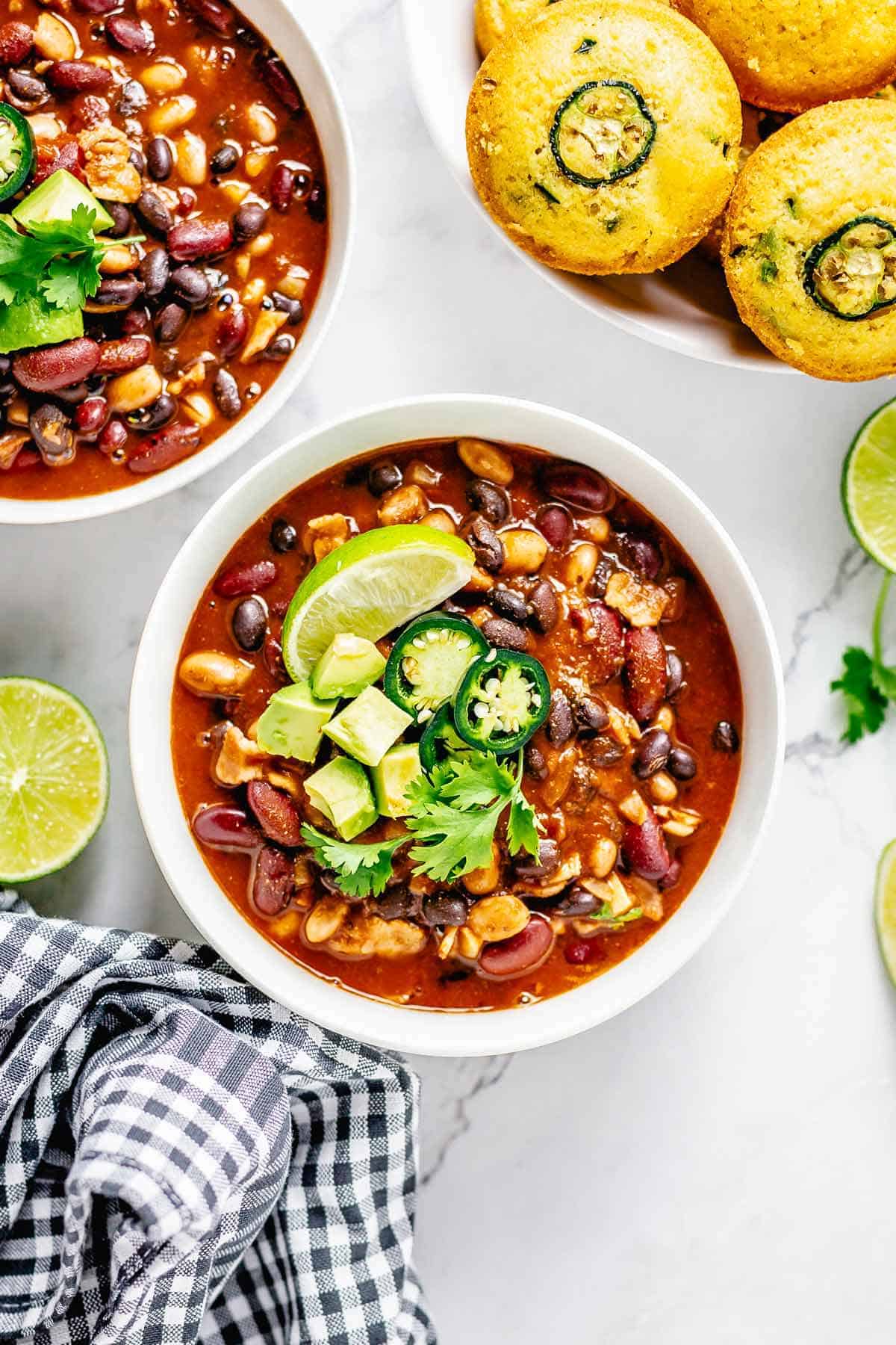 cooked beans in red sauce in a bowl with cornbread muffins and jaalpeno, cornbread, lime toppings