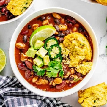 cooked beans in red sauce in a bowl with cornbread muffins and jaalpeno, cornbread, lime toppings