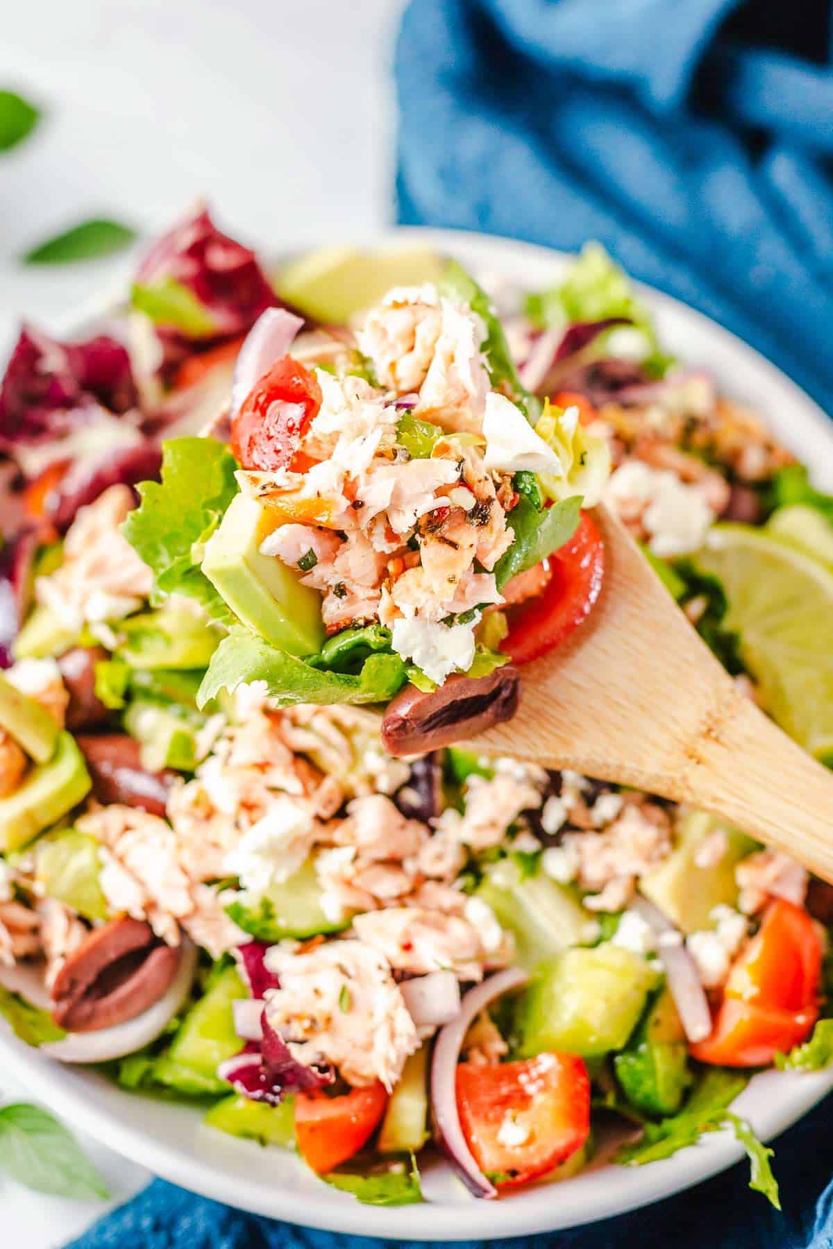 shredded cooked salmon on a wooden spoon with lettuce and vegetables