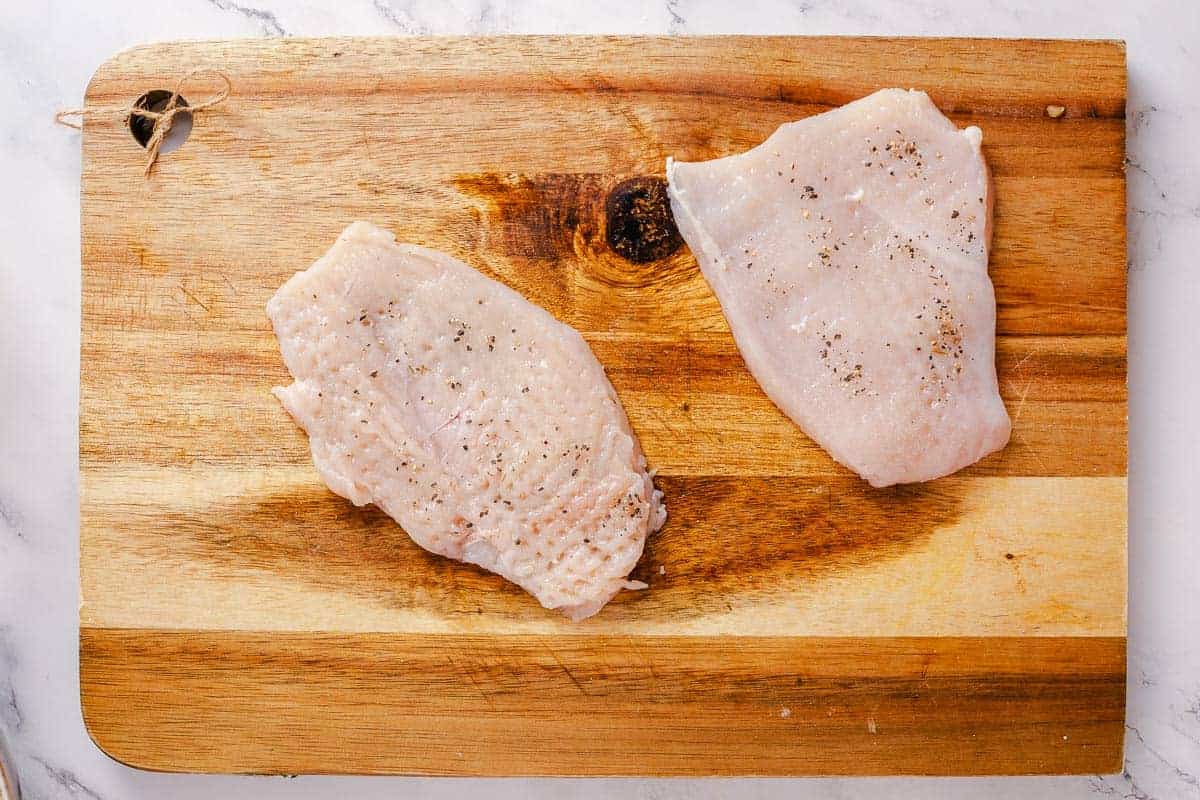 pounded and seasoned chicken breasts on a wooden borad