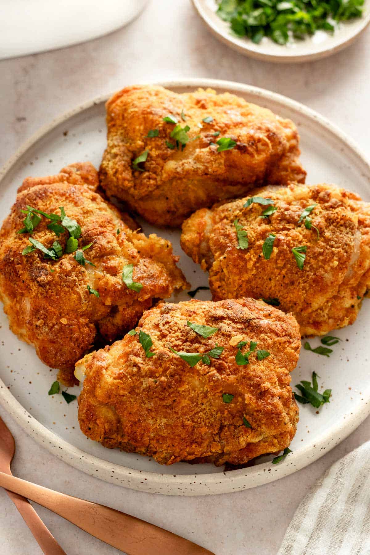 four crispy bone-in chicken thighs on a serving plate garnished with parsley.