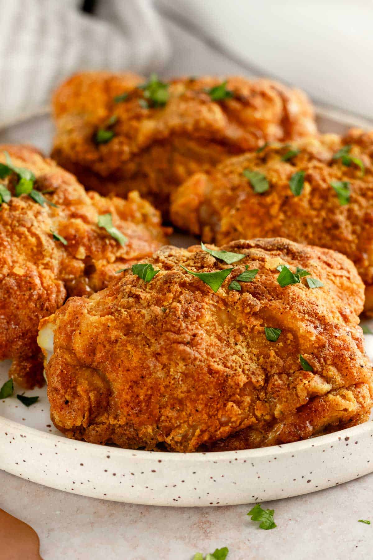 four crispy bone-in, skin-on chicken thighs on a serving plate garnished with parsley.