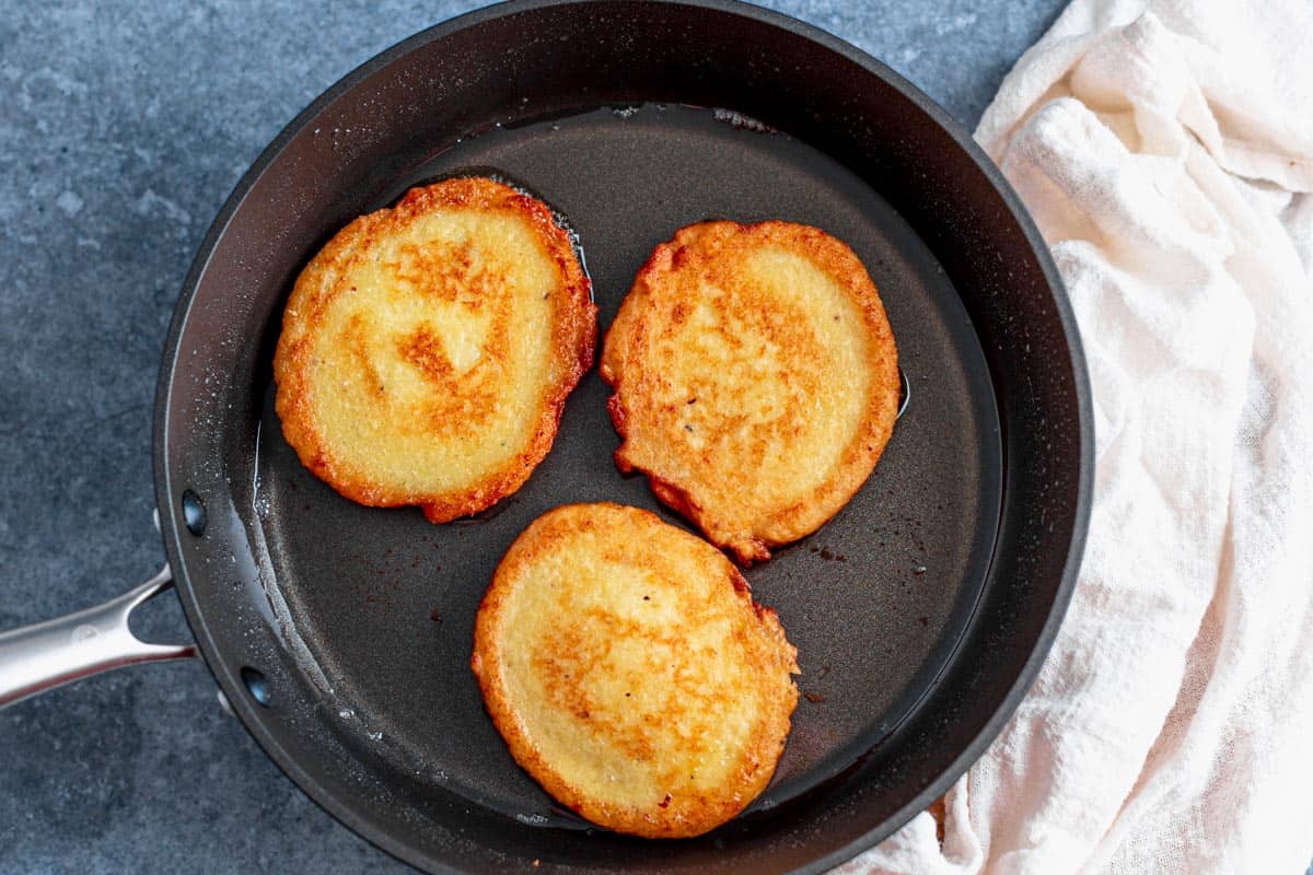 three potato pancakes cookign in pan with oil
