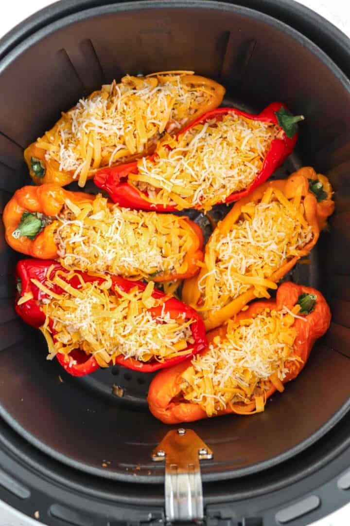 peppers topped with cheese in air fryer basket.