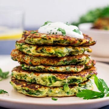 stack of zucchini fritters with a dollop of sour cream and parsley