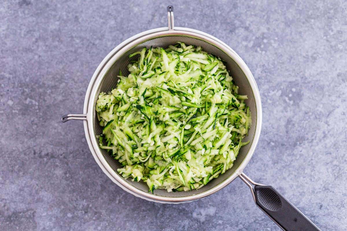 grated zucchini in a fine mesh strainer before rolling into fritters