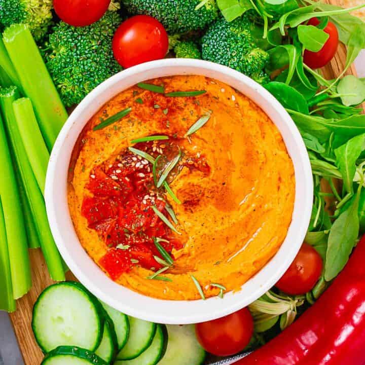 roasted pepper hummus ina bowl with toppings and green vegetables