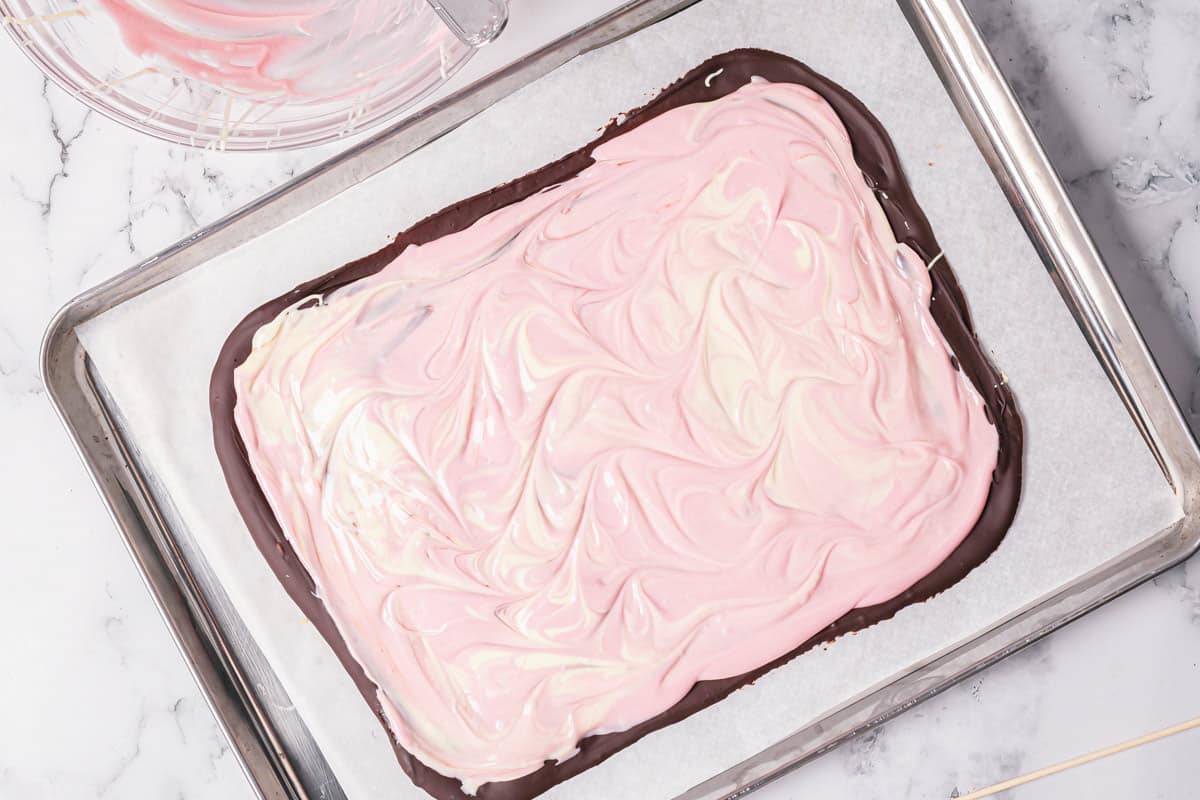 white and pink melted chocolate swirled together on top of milk chocolate bark