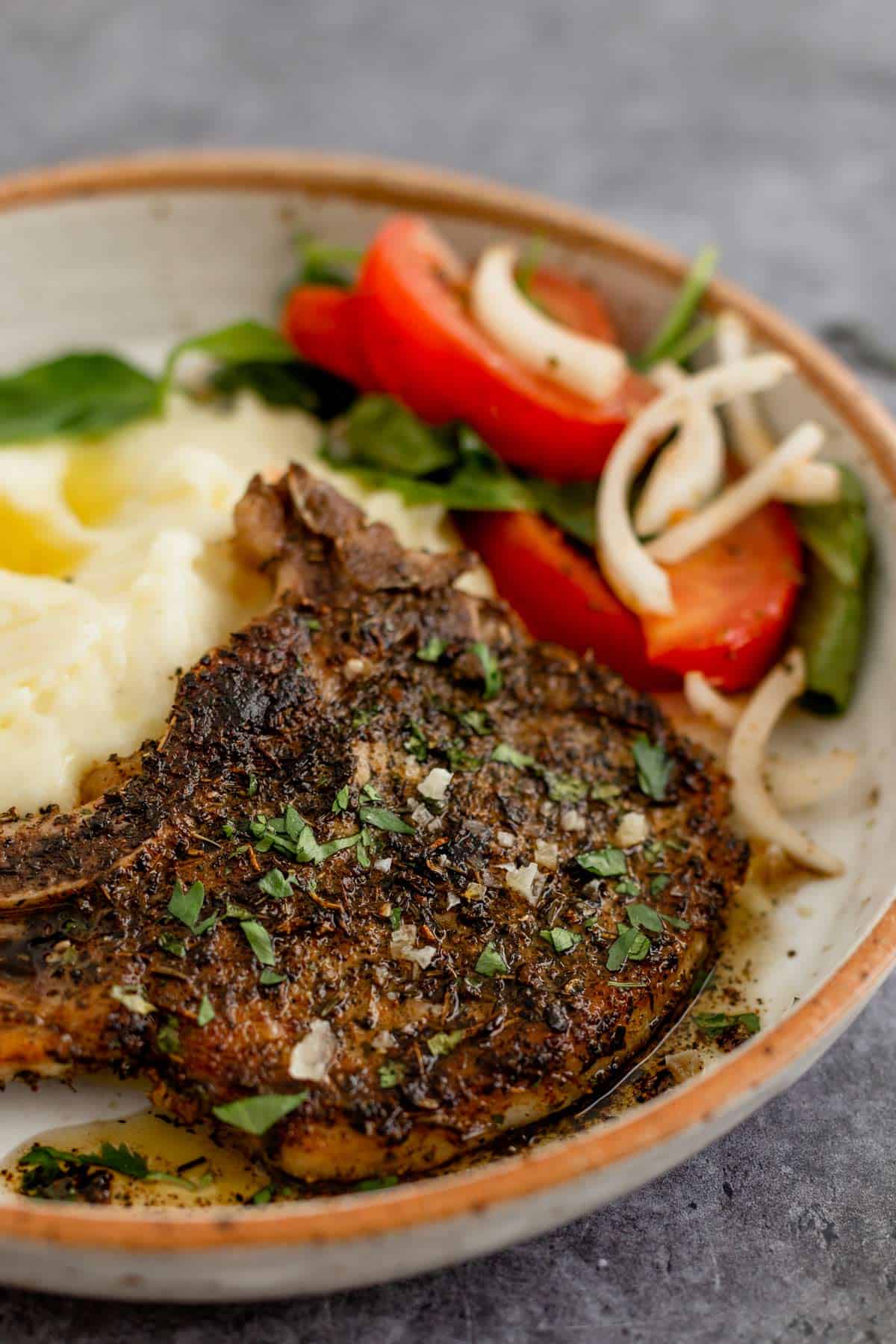 Pan Seared Pork Chop in a plate with mashed potatoes and tomato onion lettuce salad