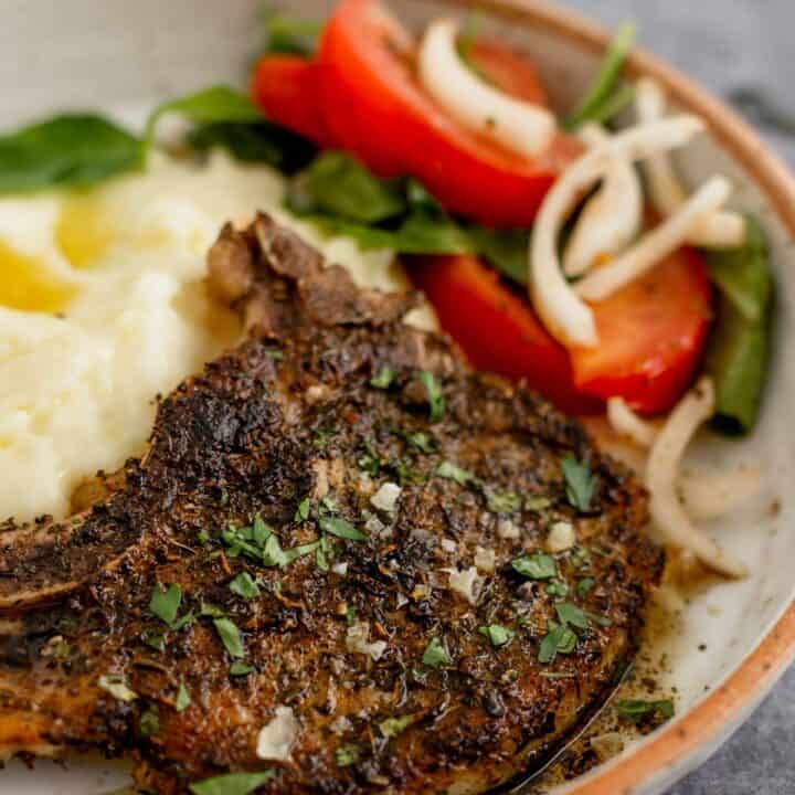 Pan Seared Pork Chop in a plate with mashed potatoes and tomato onion lettuce salad