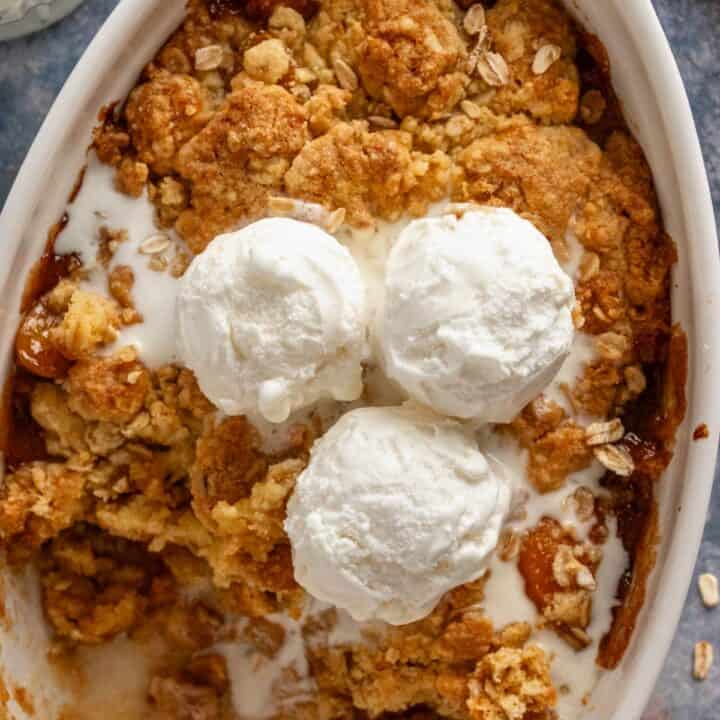 peach cobbler in oval baking dish with ice cream.