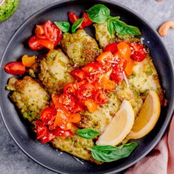 air fryer tilapia with pesto in a plate with cherry tomatoes and parmesan