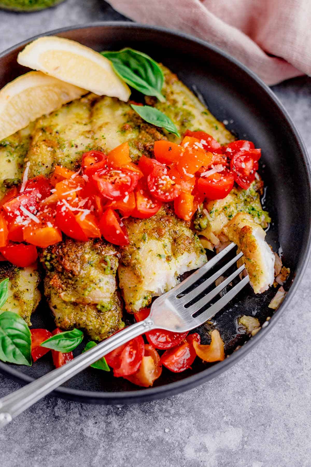 air fryer tilapia with pesto in a plate with cherry tomatoes and parmesan