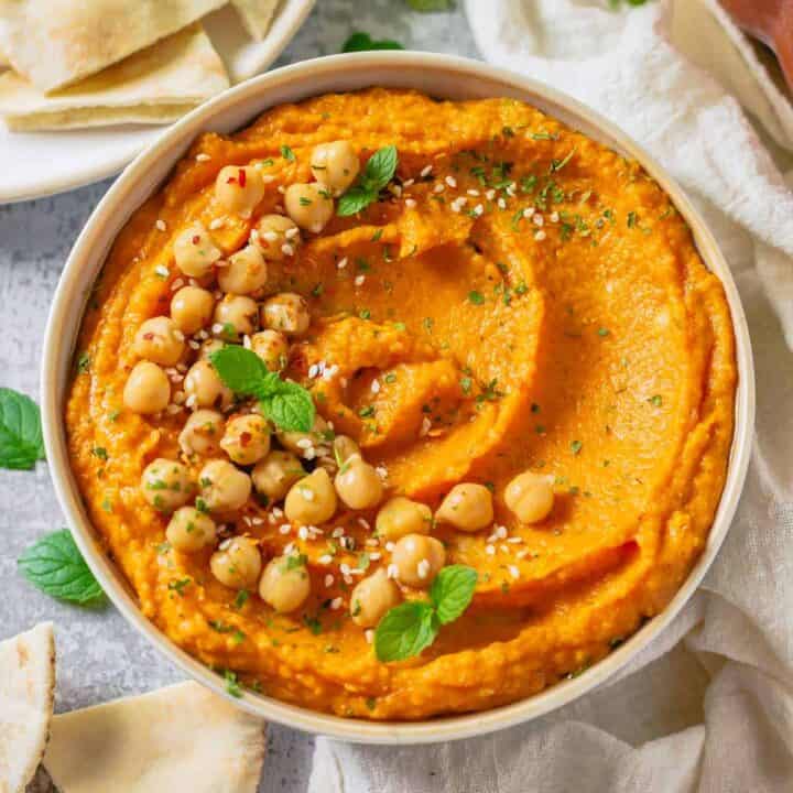 pumpkin and chickpea hummus in a white bowl on a marble table with white linen