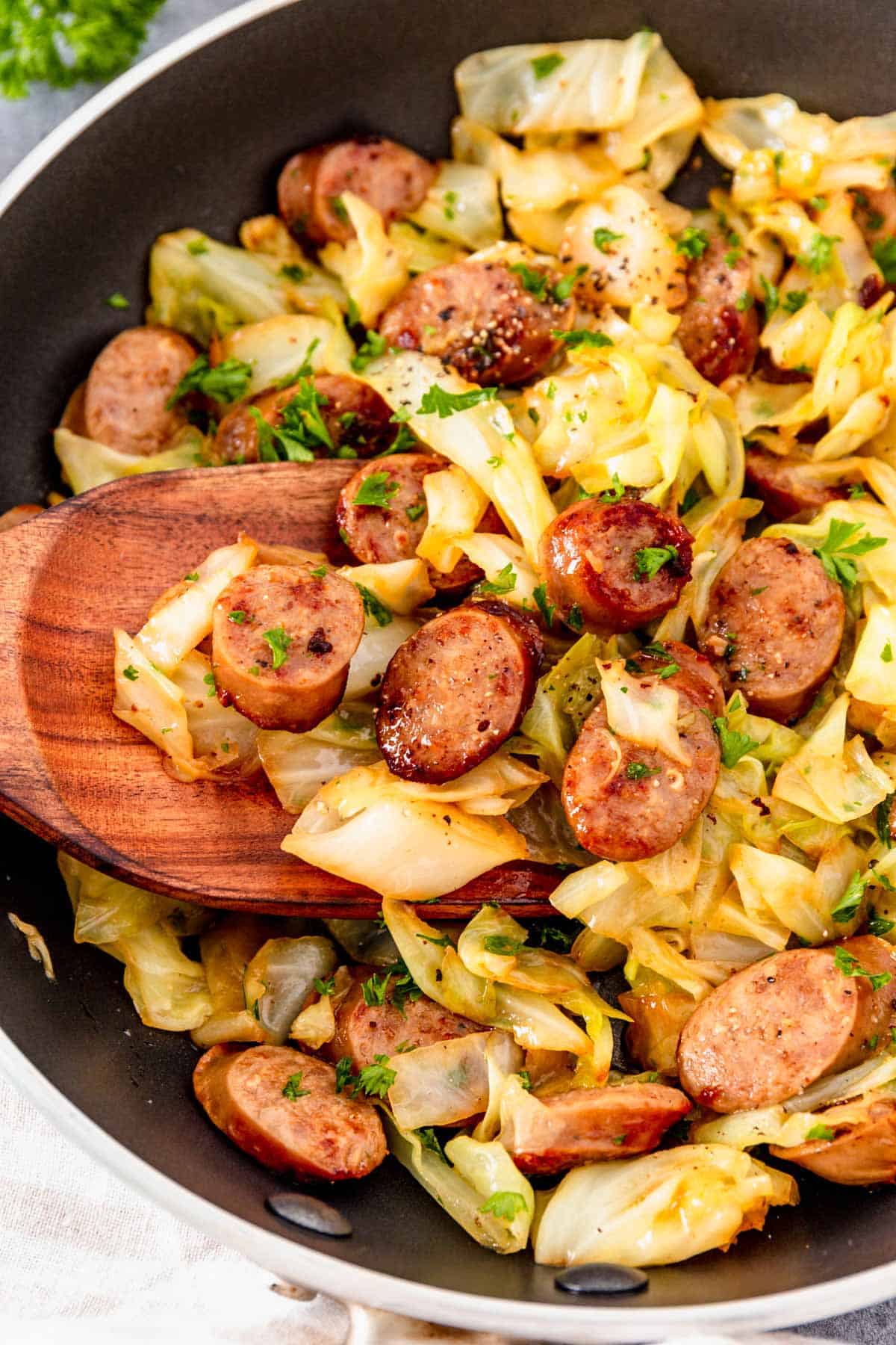 a wooden spoon in the cabbage with sausage skillet