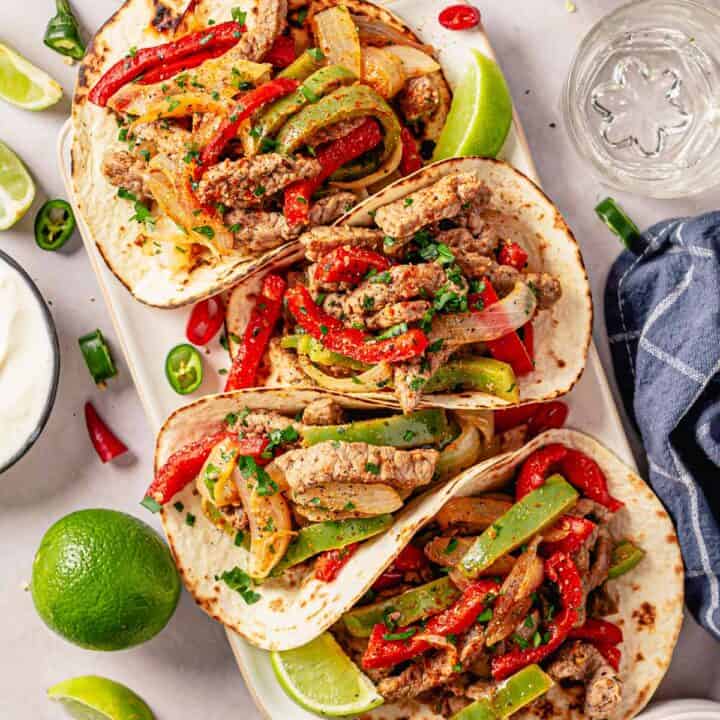 steak fajita tacos in a row with toppings and garnishes