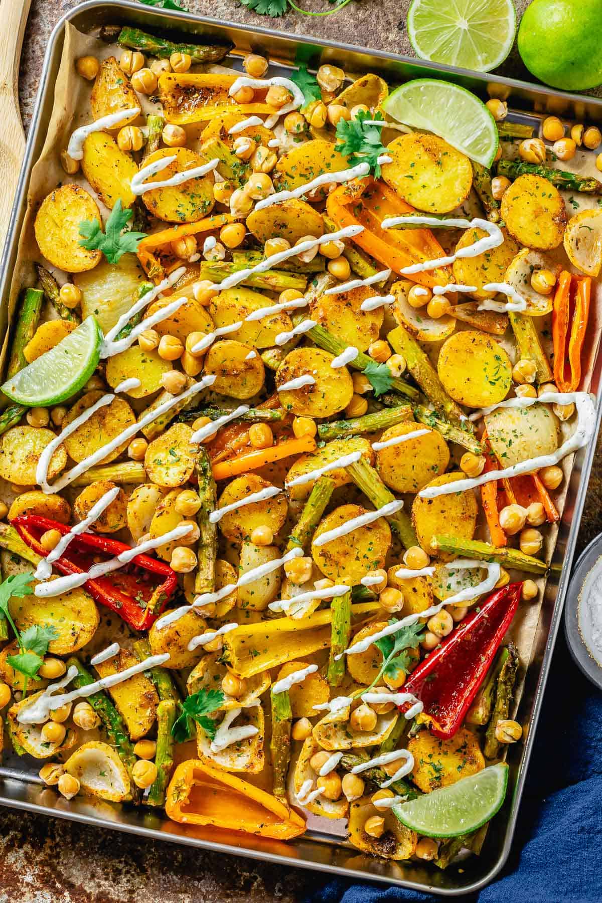 baked vegetables in a sheet pan drizzled with vegan white dressing