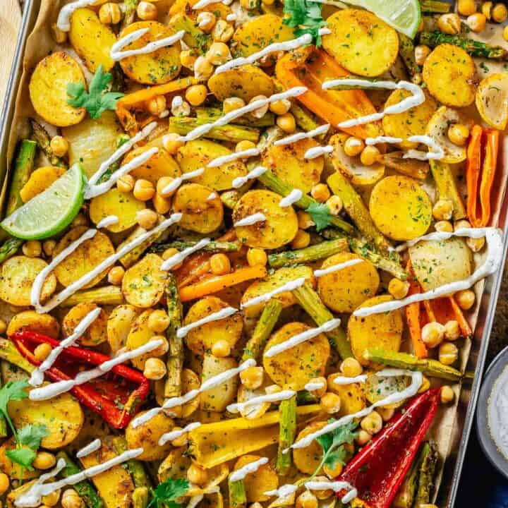 baked vegetables in a sheet pan drizzled with vegan white dressing